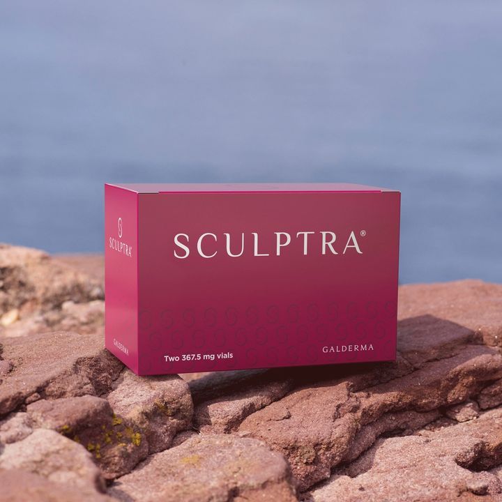 Sculptra product box in pink on rocky coast with blue water in the background, branding visible.